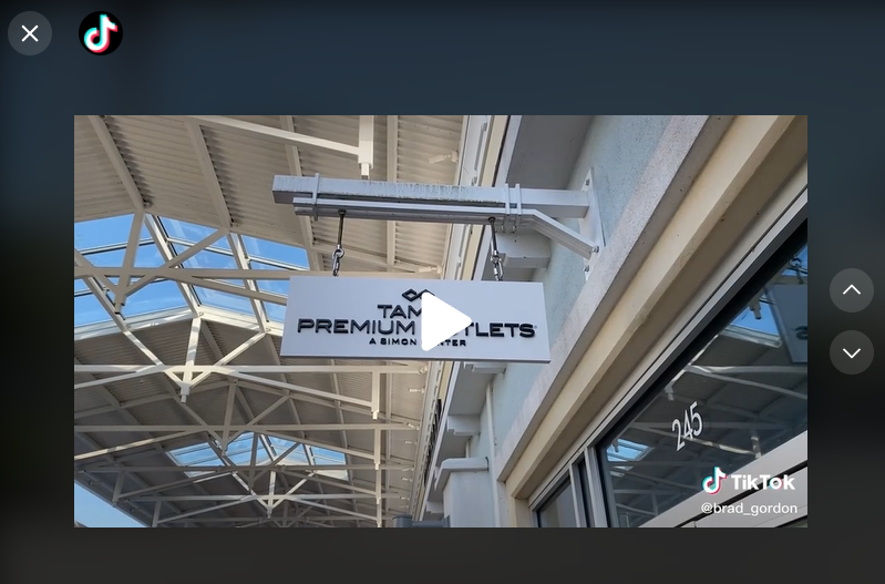 screenshot of @brad_gordon's tiktok video at the Tampa Premium Outlets, it's a sign that says tampa premium outlets hanging off the side of a building under the covered walkway